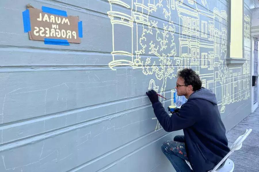 Un artiste peint une fresque murale sur le côté d'un bâtiment du Mission District, avec une pancarte collée sur le bâtiment indiquant « Peinture murale en cours ». San Francisco, Californie.