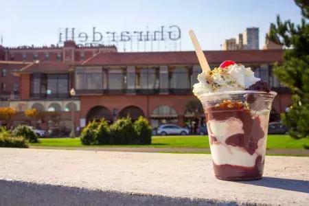 A chocolate sundae sits in the foreground with Ghirardelli Square in the background.